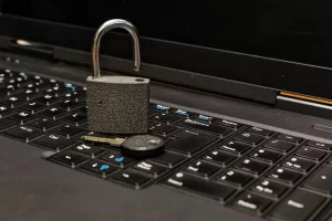 A imagem mostra um cadeado aberto colocado sobre um teclado de laptop. Ao lado do cadeado, há uma chave, simbolizando a segurança e a proteção de dados. O cadeado aberto pode representar vulnerabilidades, sugerindo a importância de proteger as informações digitais. Essa composição é frequentemente utilizada em contextos relacionados à segurança da informação, destacando a necessidade de práticas eficazes para manter a privacidade e a integridade dos dados em um ambiente digital