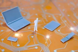 A imagem apresenta uma cena simbólica com miniaturas de um laptop, um tablet, e um celular, posicionados sobre uma base com padrão de circuito eletrônico, sugerindo um contexto de tecnologia e dados. Uma pequena figura humana, em pé e pensativa, observa esses dispositivos, o que pode representar uma reflexão ou decisão em torno da digitalização, comunicação ou migração de dados empresariais, com foco em tecnologias e soluções digitais. Essa configuração sugere um cenário relacionado à modernização e à integração de diferentes dispositivos no ambiente corporativo.