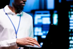 A imagem mostra um profissional usando um laptop em um ambiente de servidores, com uma iluminação voltada para um ambiente de tecnologia. A presença de um crachá sugere que ele é um gestor ou responsável por TI, possivelmente lidando com configurações de segurança ou monitoramento. A cena pode representar a aplicação de medidas de segurança, como a utilização de uma VPN para restringir o acesso a sistemas e dados sensíveis, protegendo a rede e controlando quem pode acessar determinadas informações